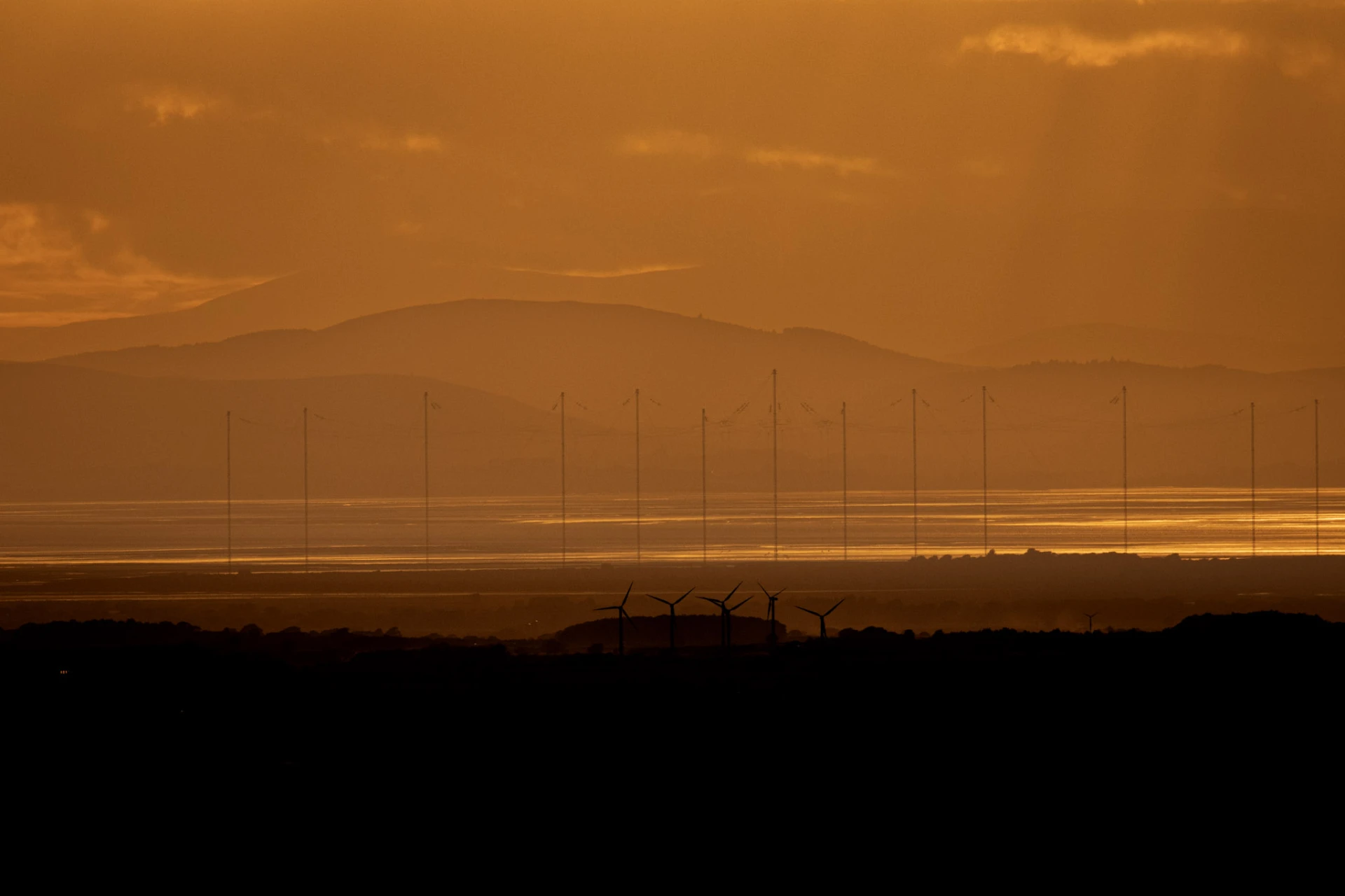 Wind turbines silhouetted against layered mountains at golden hour